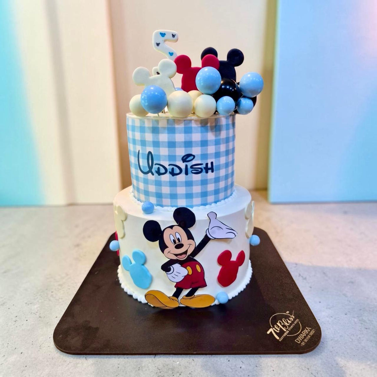 Eggless two-tier Mickey Mouse birthday cake with blue gingham top tier and balloon topper, 7th Bliss Dwarka Delhi